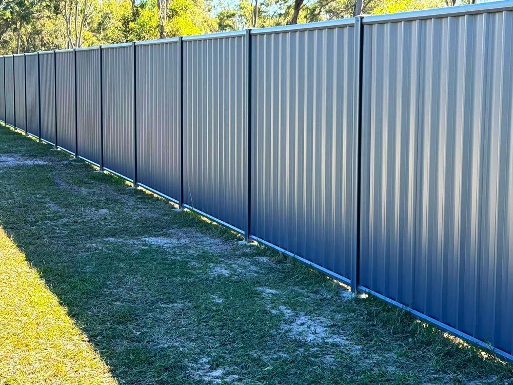 A Blue Metal Fence is Sitting on Top of a Lush Green Field — Brendan's Landscaping and Fencing In Bundaberg, QLD