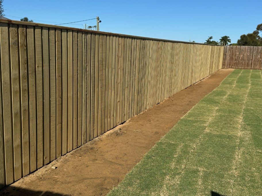 A Wooden Fence Surrounds a Lush Green Field — Brendan's Landscaping and Fencing In Coral Cove, QLD
