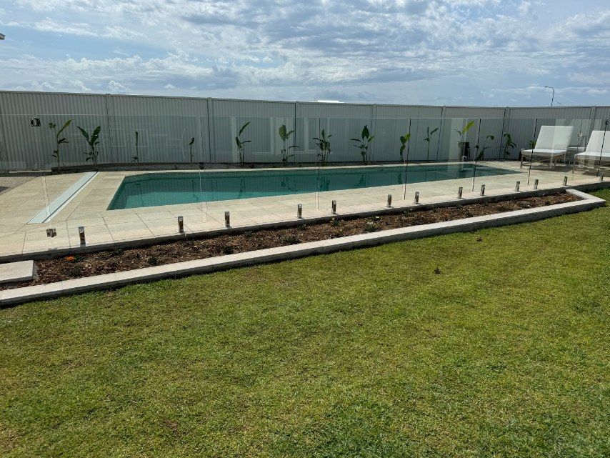 Swimming Pool is Surrounded by a Fence and a Lush Green Lawn  — Brendan's Landscaping and Fencing In Bundaberg, QLD