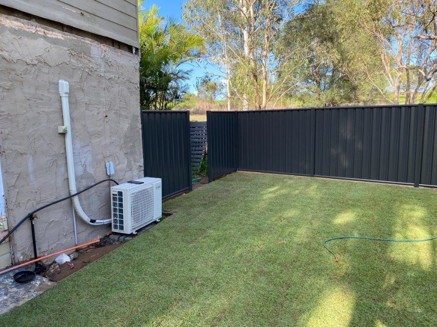 A Backyard With a Black Fence and a White Air Conditioner — Brendan's Landscaping and Fencing In Bundaberg, QLD