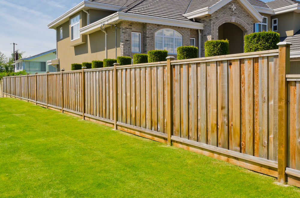 A Wooden Fence Surrounds a Lush Green Lawn in Front of a House — Brendan's Landscaping and Fencing In Bundaberg, QLD