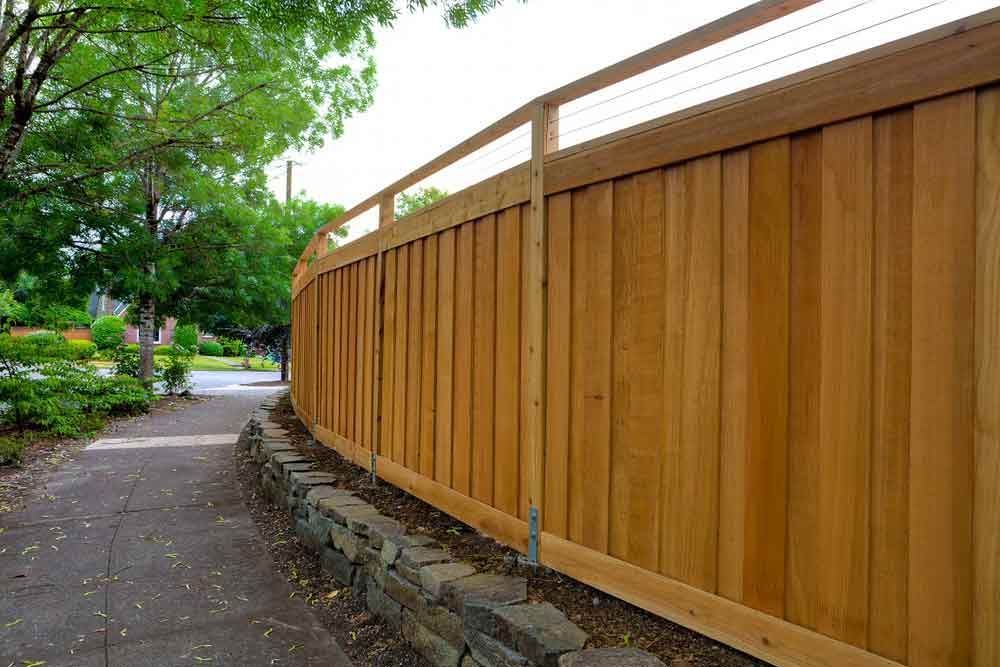 A Wooden Fence Along a Sidewalk Next to a Stone Wall — Brendan's Landscaping and Fencing In Bundaberg, QLD