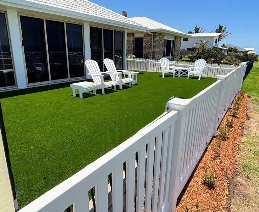 A White Fence Surrounds a Lawn With Chairs in Front of a House — Brendan's Landscaping and Fencing In Bundaberg, QLD