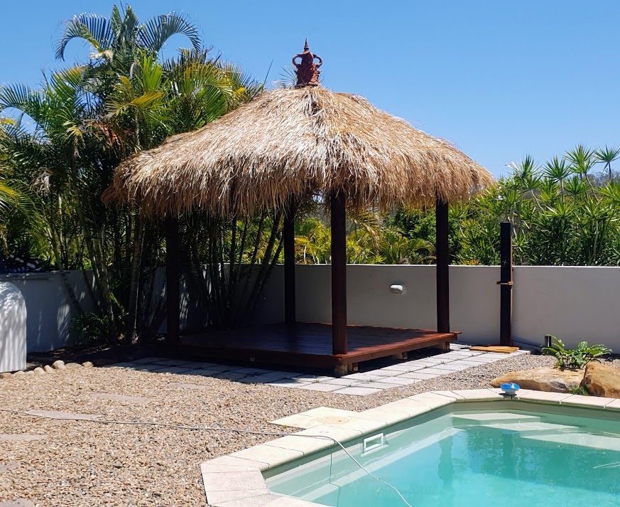 A Wooden Deck With a Swimming Pool in the Background — Brendan's Landscaping and Fencing In Bundaberg, QLD