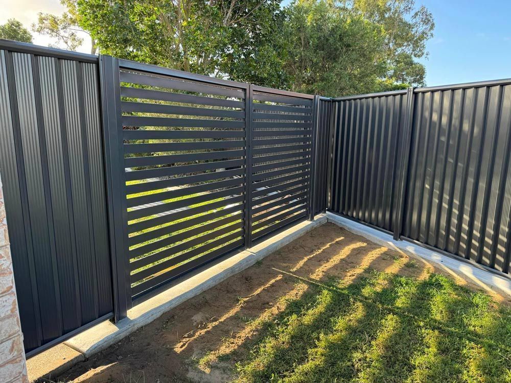 A Black Fence is Surrounding a Lush Green Yard — Brendan's Landscaping and Fencing In Bundaberg, QLD