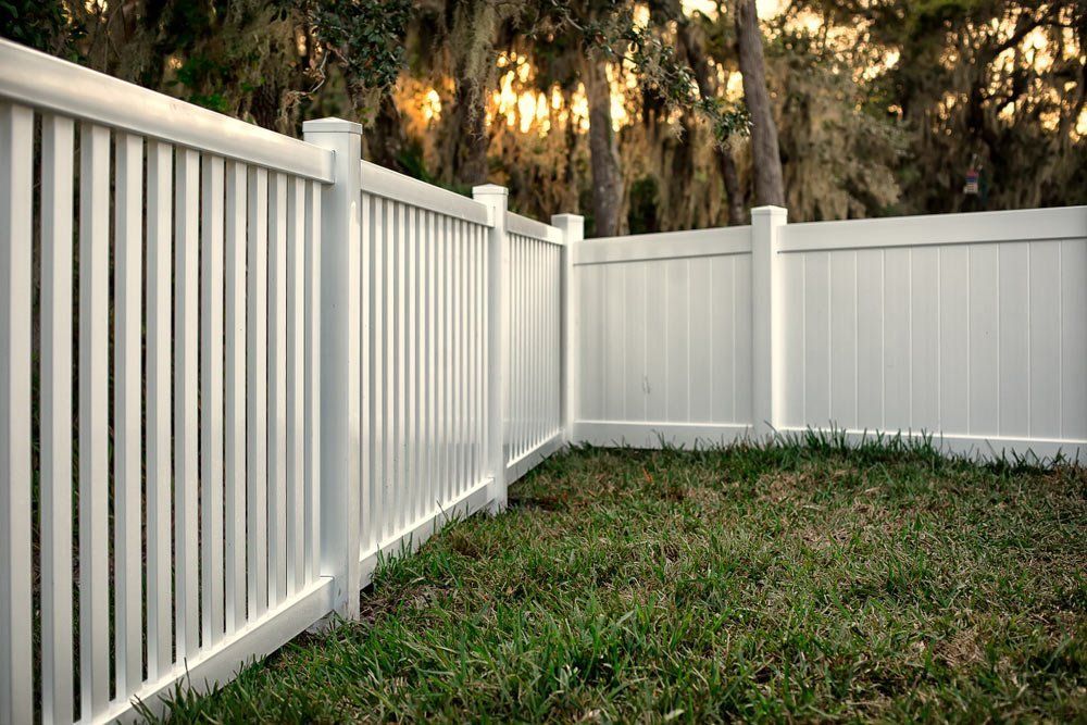 A White Vinyl Fence Surrounds a Lush Green Yard — Brendan's Landscaping and Fencing In Bundaberg, QLD