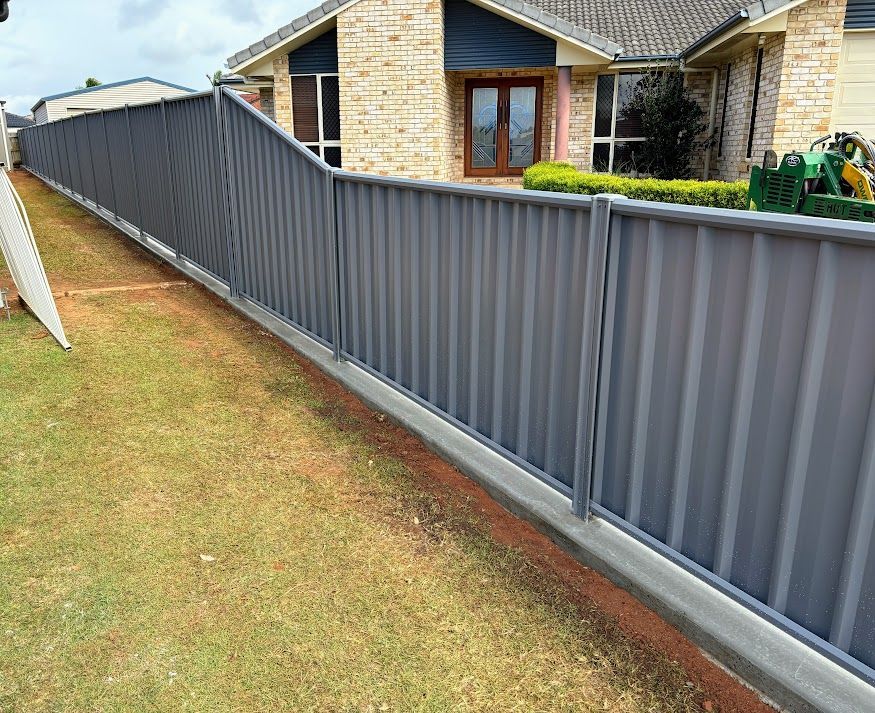 A Brown Fence With Yellow Pillars is Surrounded by Grass and Gravel — Brendan's Landscaping and Fencing In Bundaberg, QLD