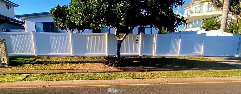 A White Fence Surrounds a House With a Tree in Front of It — Brendan's Landscaping and Fencing In Bundaberg, QLD