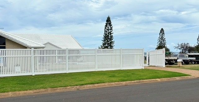 A White Fence Surrounds a House With a Truck Parked in Front of It — Brendan's Landscaping and Fencing In Bundaberg, QLD