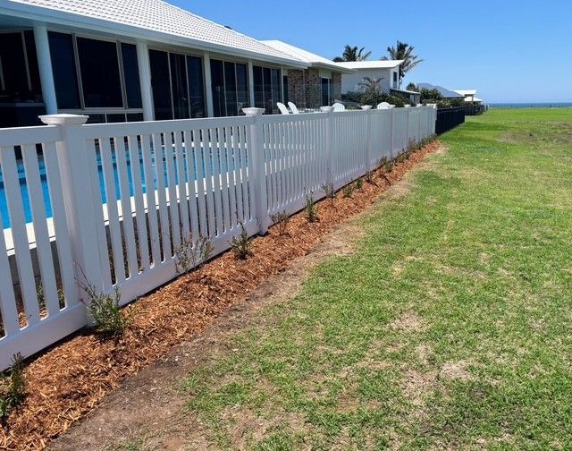 A White Fence Surrounds a Swimming Pool in Front of a — Brendan's Landscaping and Fencing In Bundaberg, QLD
