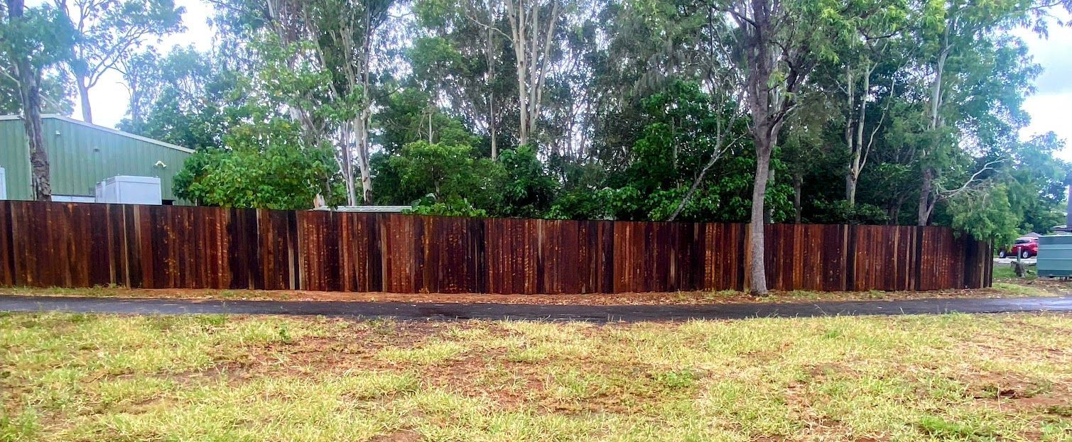 A Wooden Fence Surrounds a Grassy Field With Trees in the Background — Brendan's Landscaping and Fencing In Bundaberg, QLD