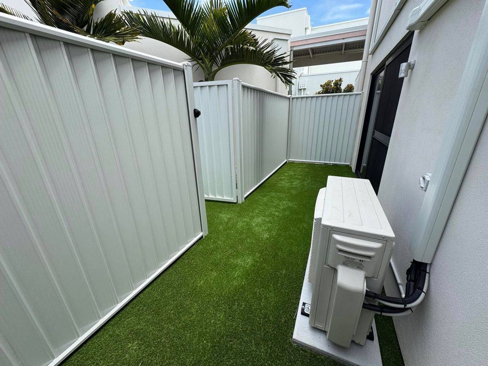 White Fence and a White Air Conditioner on the Side of the House — Brendan's Landscaping and Fencing In Bundaberg, QLD
