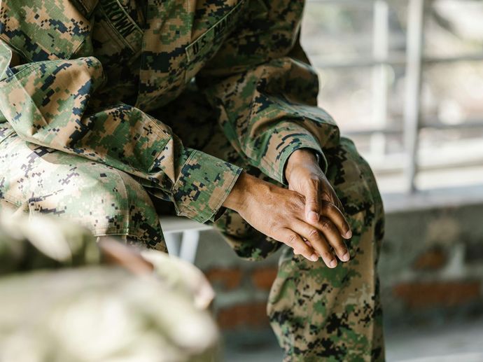 A soldier is sitting on a bench with his hands on his knees.
