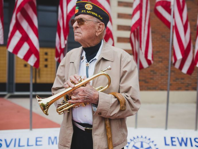 An elderly man is playing a trumpet in front of american flags