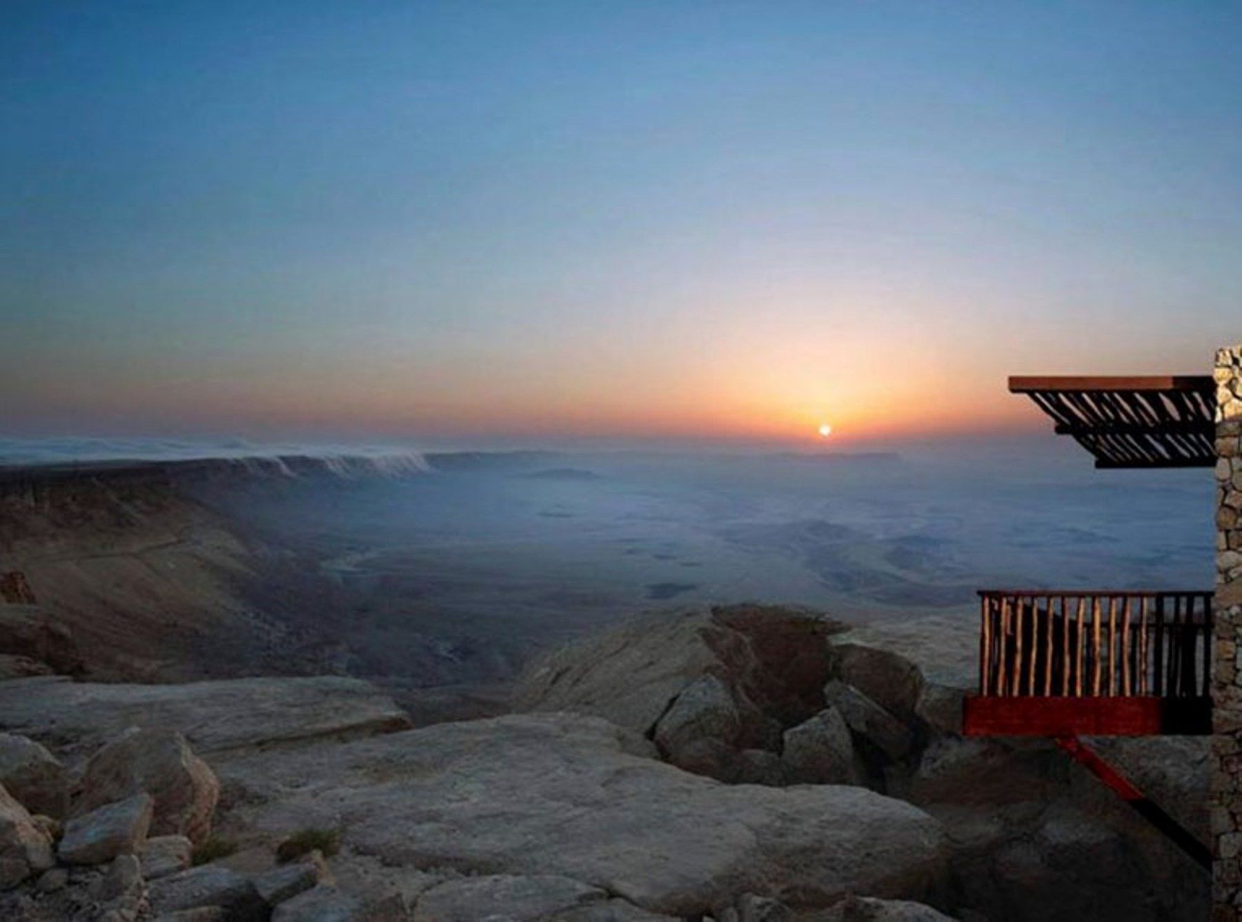 השמש שוקעת מעל עמק עם מרפסת בחזית.