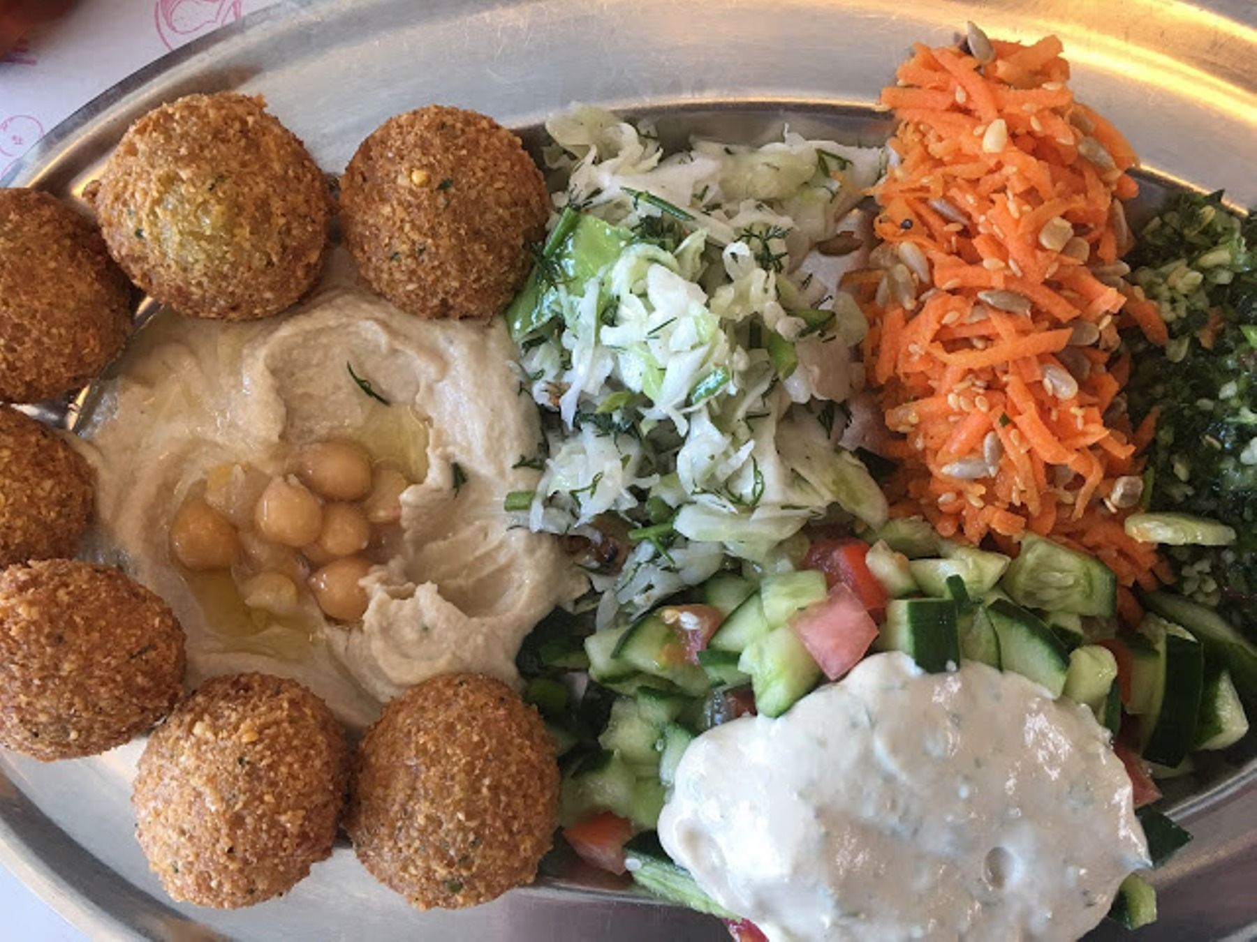 צלחת אוכל עם פלאפל, חומוס, גזר וירקות על שולחן.