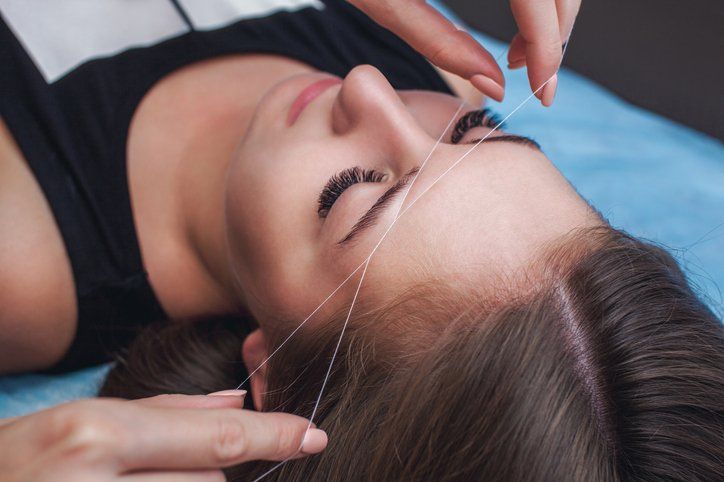 A woman is getting her eyebrows threaded in a beauty salon.