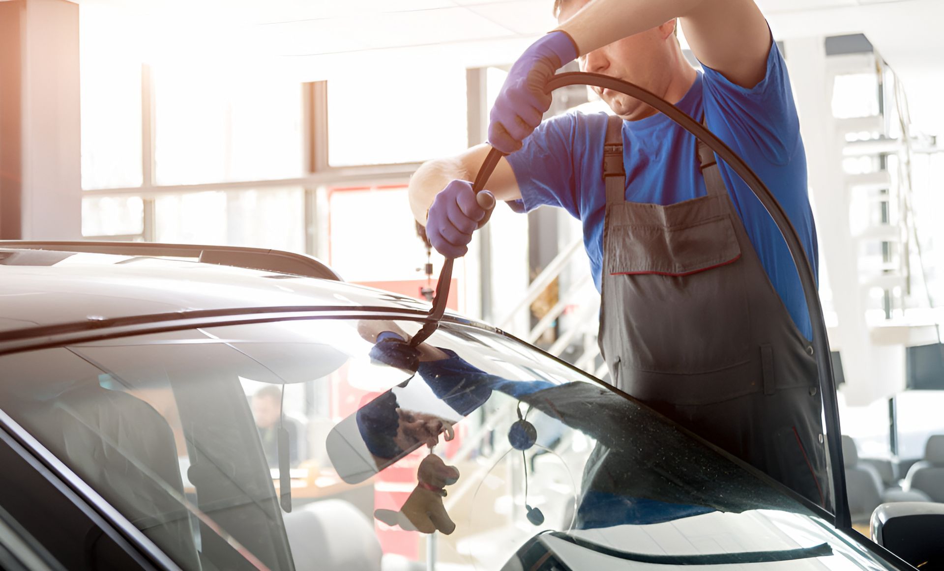 A Man Is Fixing A Windshield On A Car In A Garage — Canberra Windscreens In Fyshwick, ACT