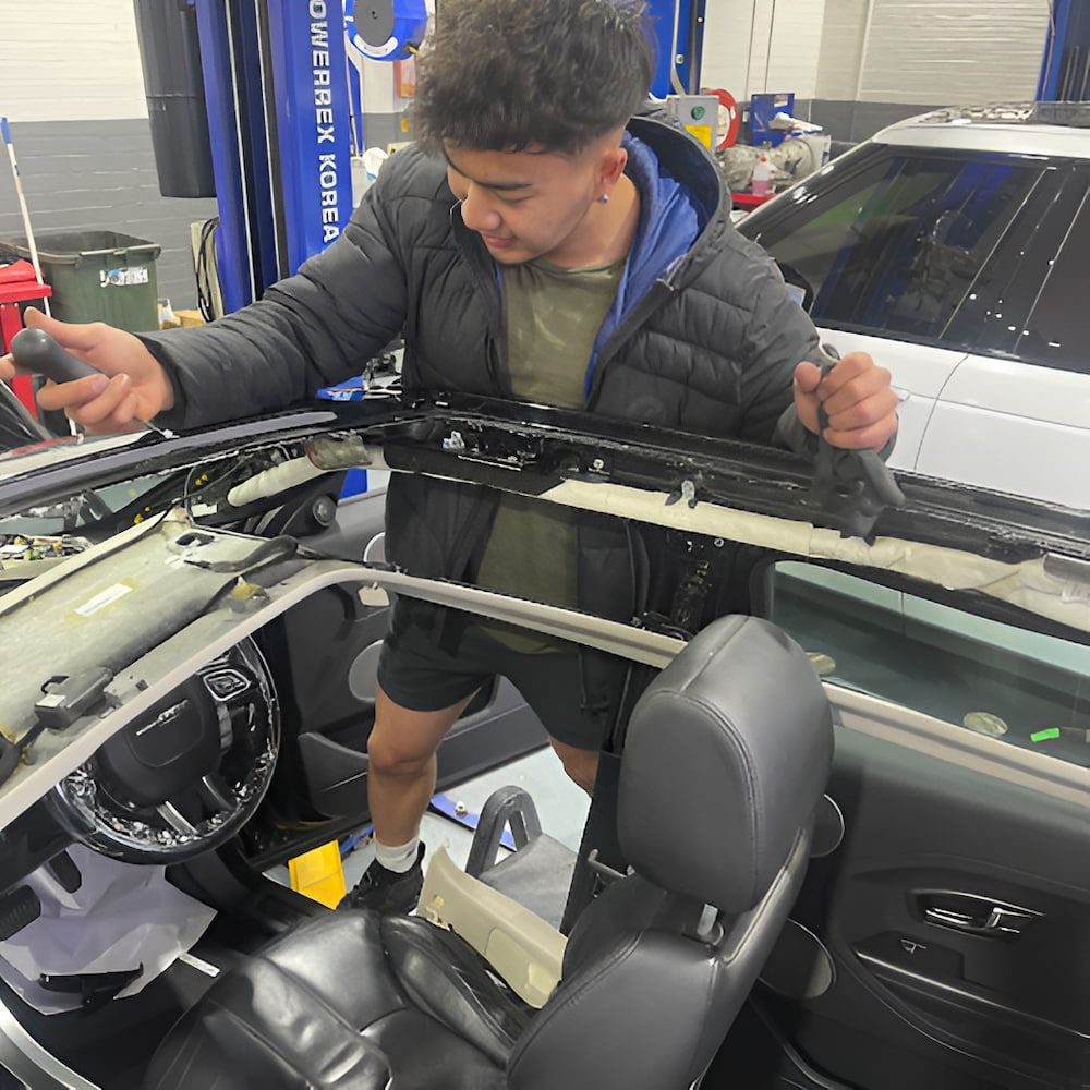 A Man Is Working On The Roof Of A Car In A Garage — Canberra Windscreens In Conder, ACT