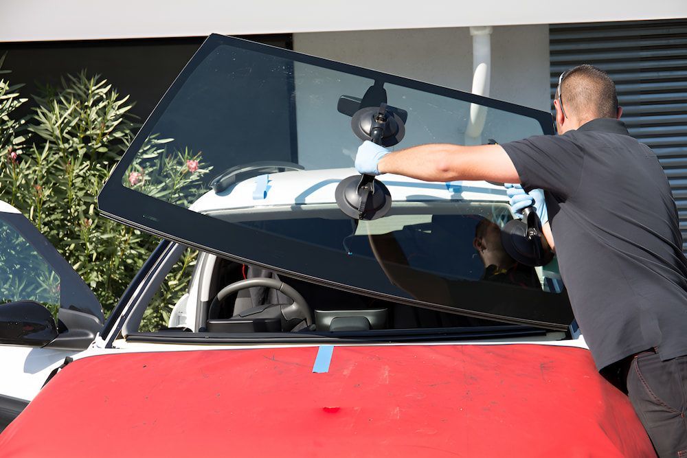 A Man Is Installing A Windshield On A Red Car — Canberra Windscreens In Conder, ACT