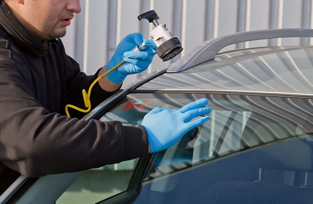 A Man Wearing Blue Gloves Is Fixing A Windshield On A Car — Canberra Windscreens In Tuggeranong, ACT