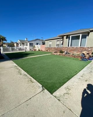A house with green artificial turf lawn, sidewalk in foreground, sunny day.