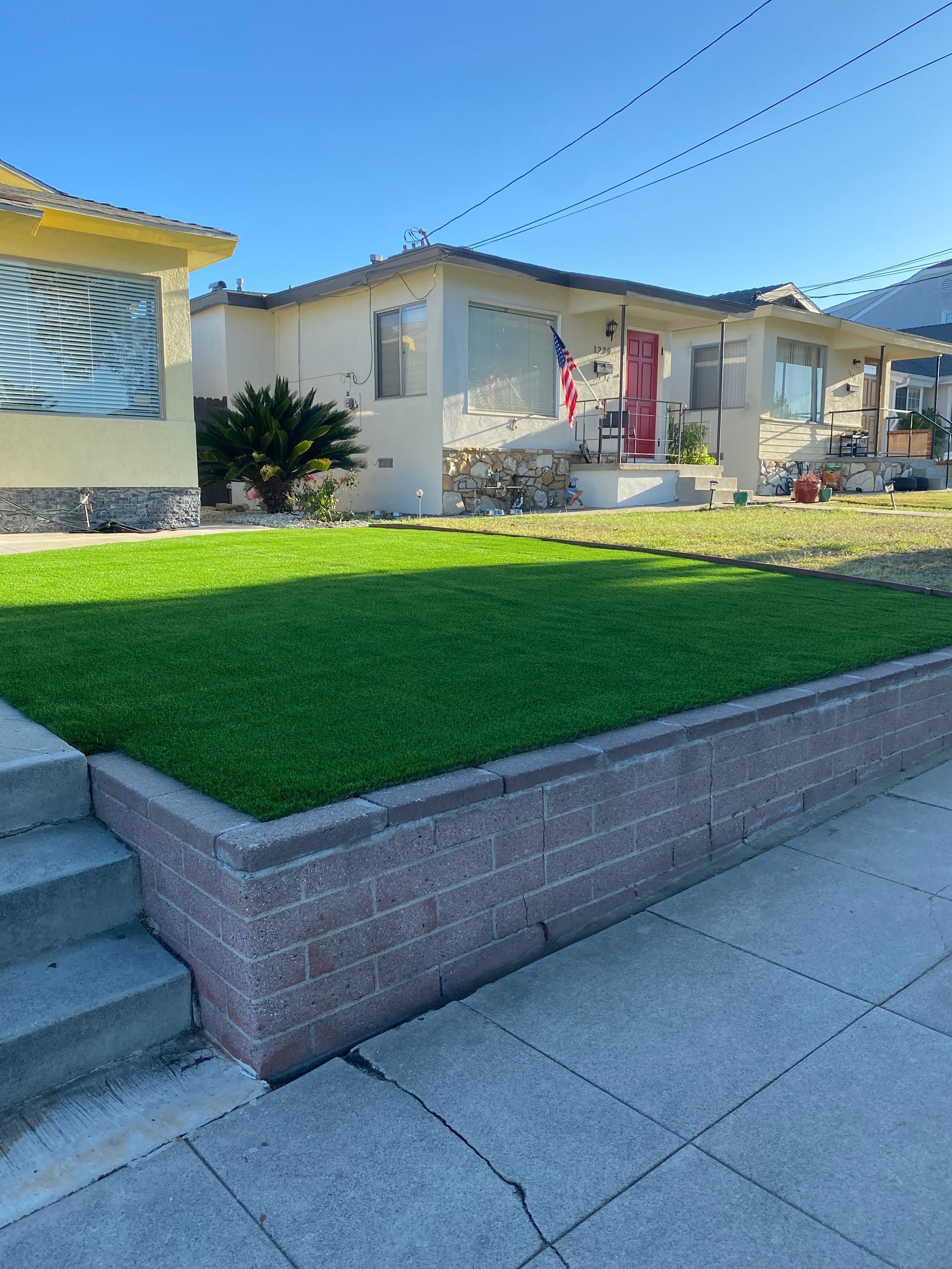 A house with a red door and a neat lawn, raised by a retaining wall.