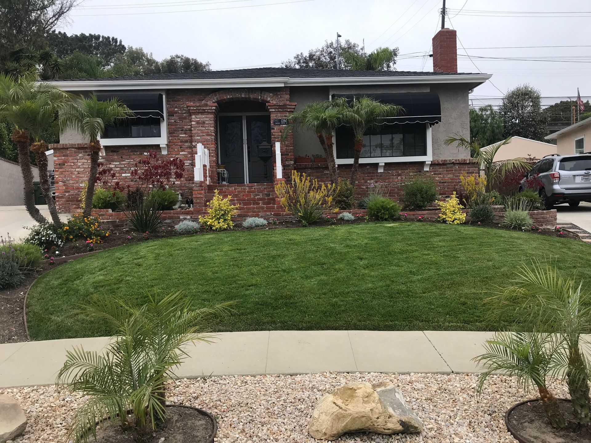 Small brick and stucco house with well-manicured lawn and landscaping on a cloudy day.