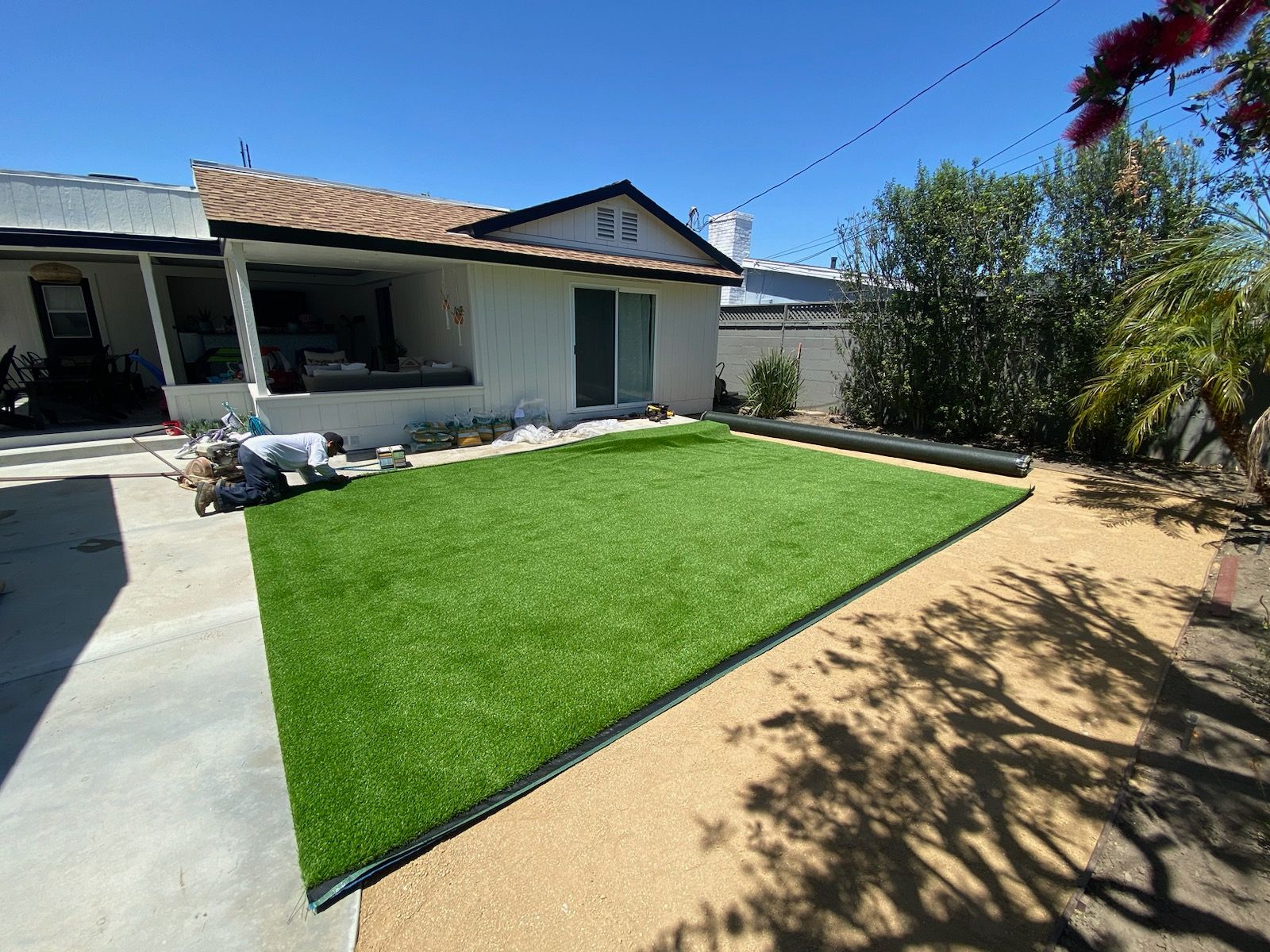 Backyard with green artificial turf, tan gravel, and a white house with a sliding glass door.