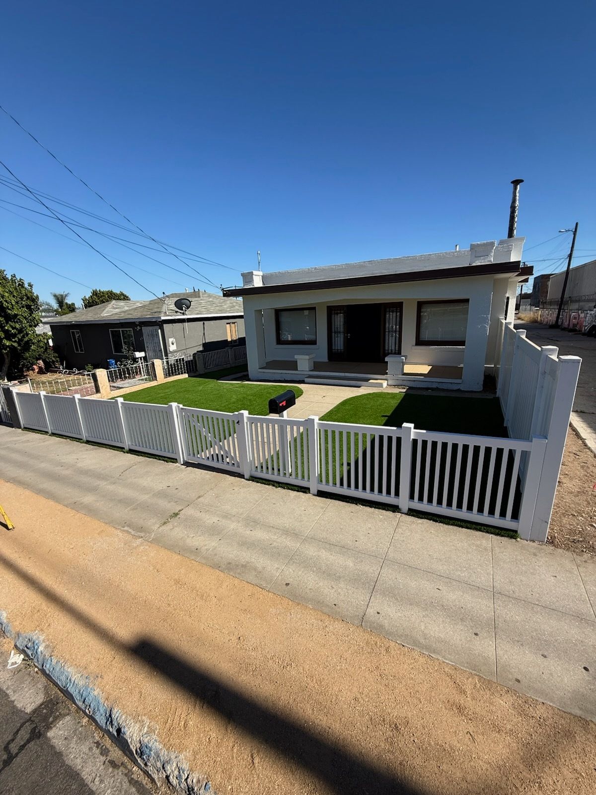 White house with a white picket fence, front yard with green grass, and a clear blue sky.