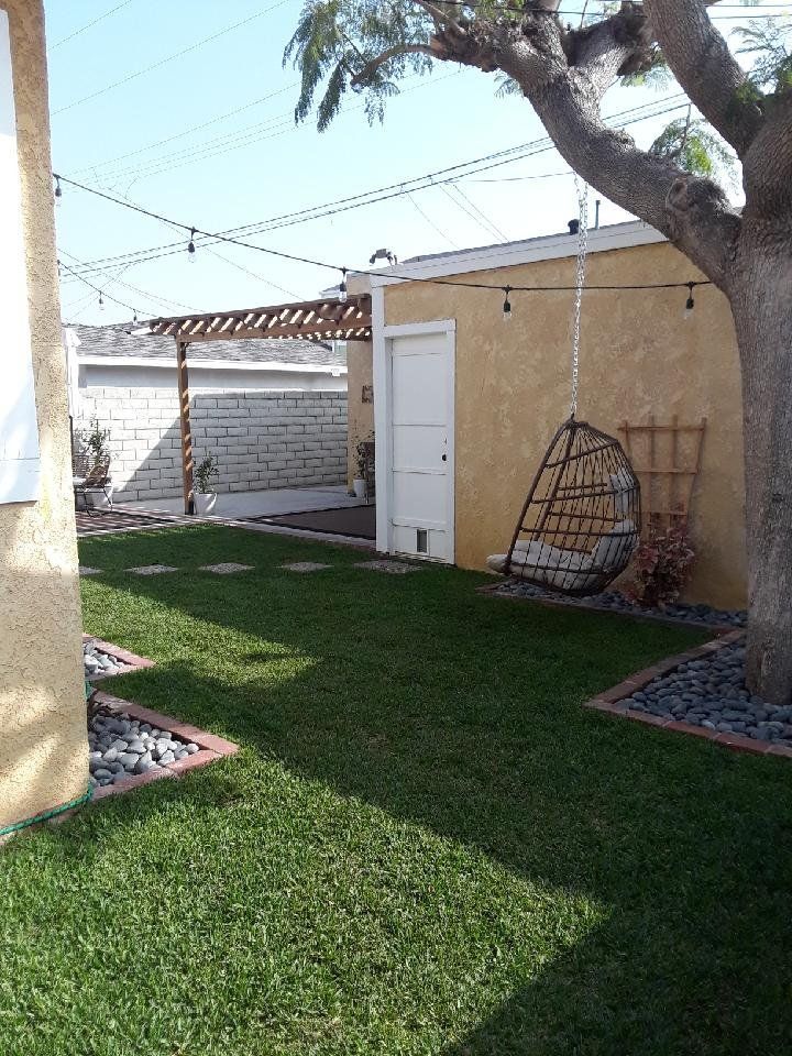 A backyard with green grass, a hanging chair, and a yellow stucco building under a sunny sky.