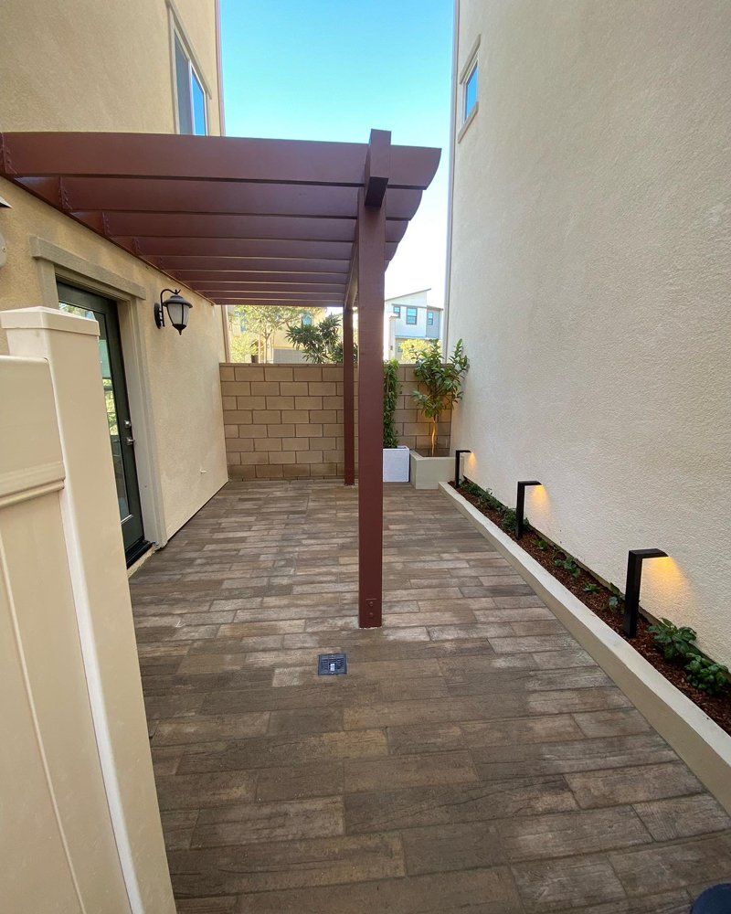 Patio with pergola, brick pavers, and pathway lighting between beige walls.