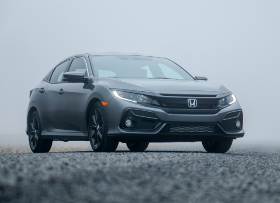 A honda civic hatchback is parked on the side of a road in the fog.