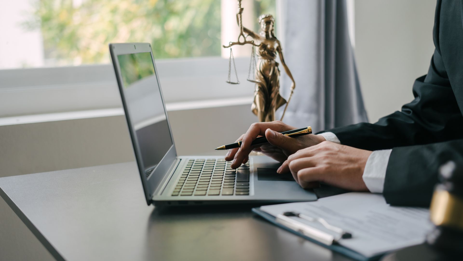 A man is typing on a laptop computer with a statue of justice in the background.