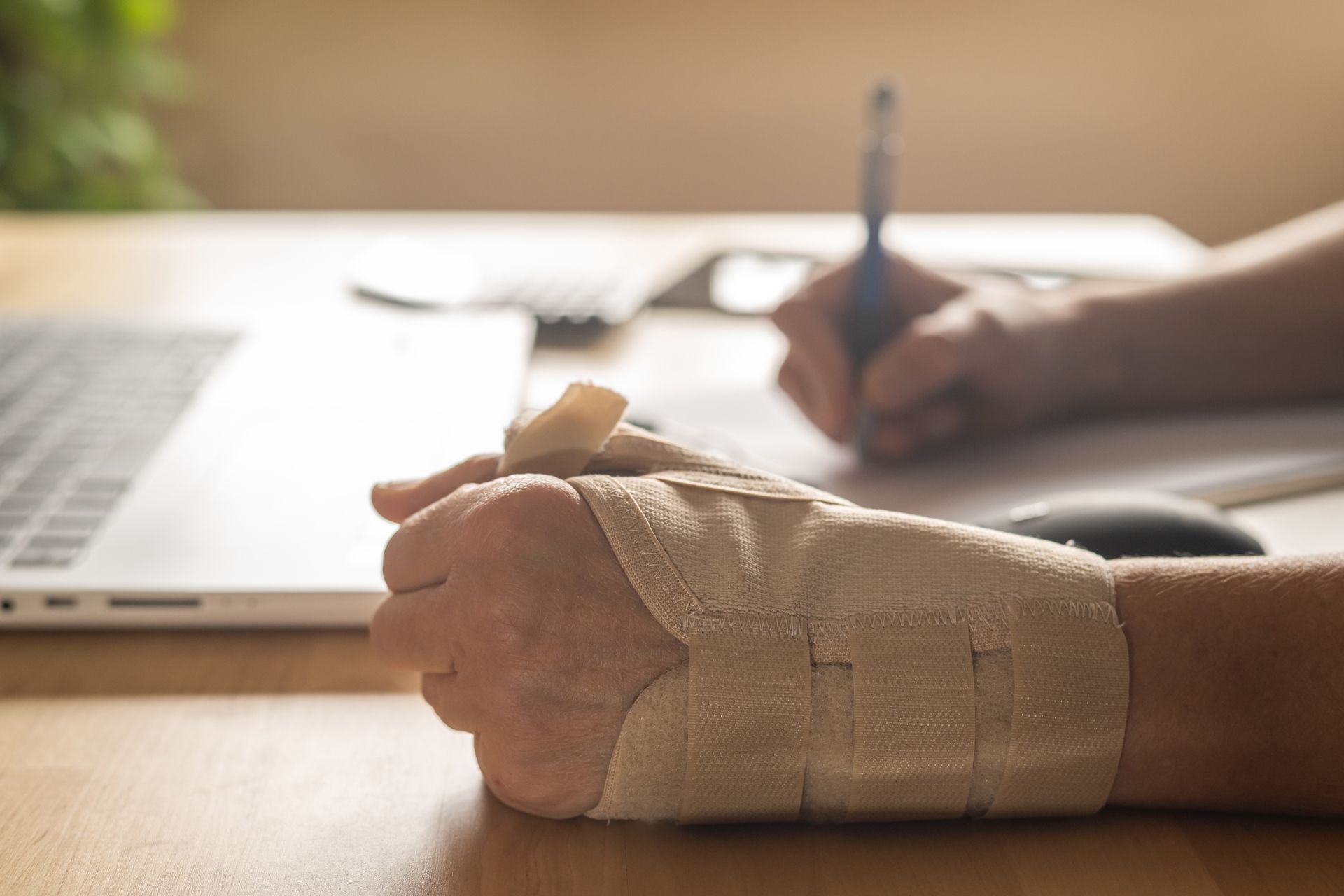 A person with a bandaged wrist is writing on a piece of paper.