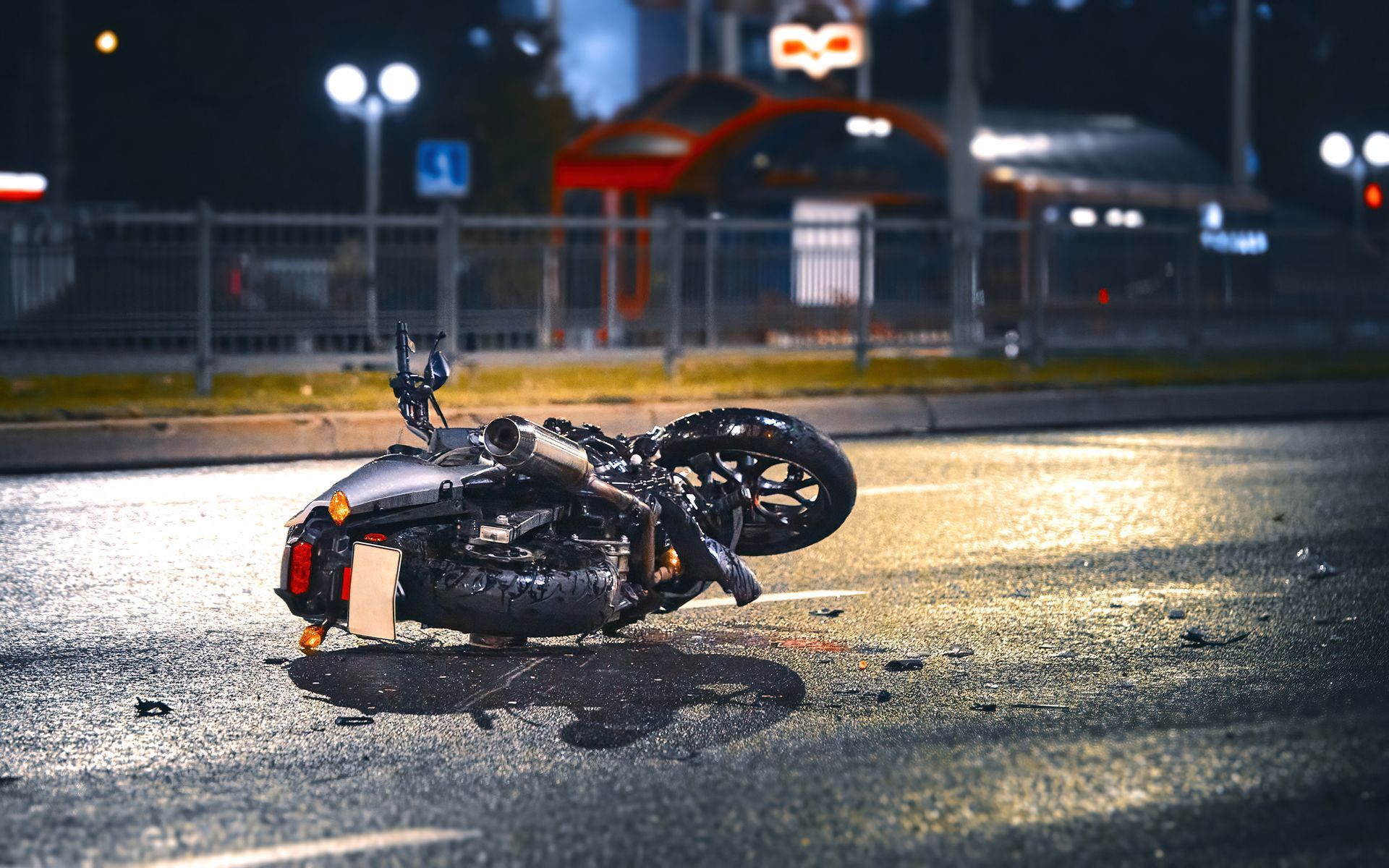 A motorcycle has crashed into a car on the side of the road at night.