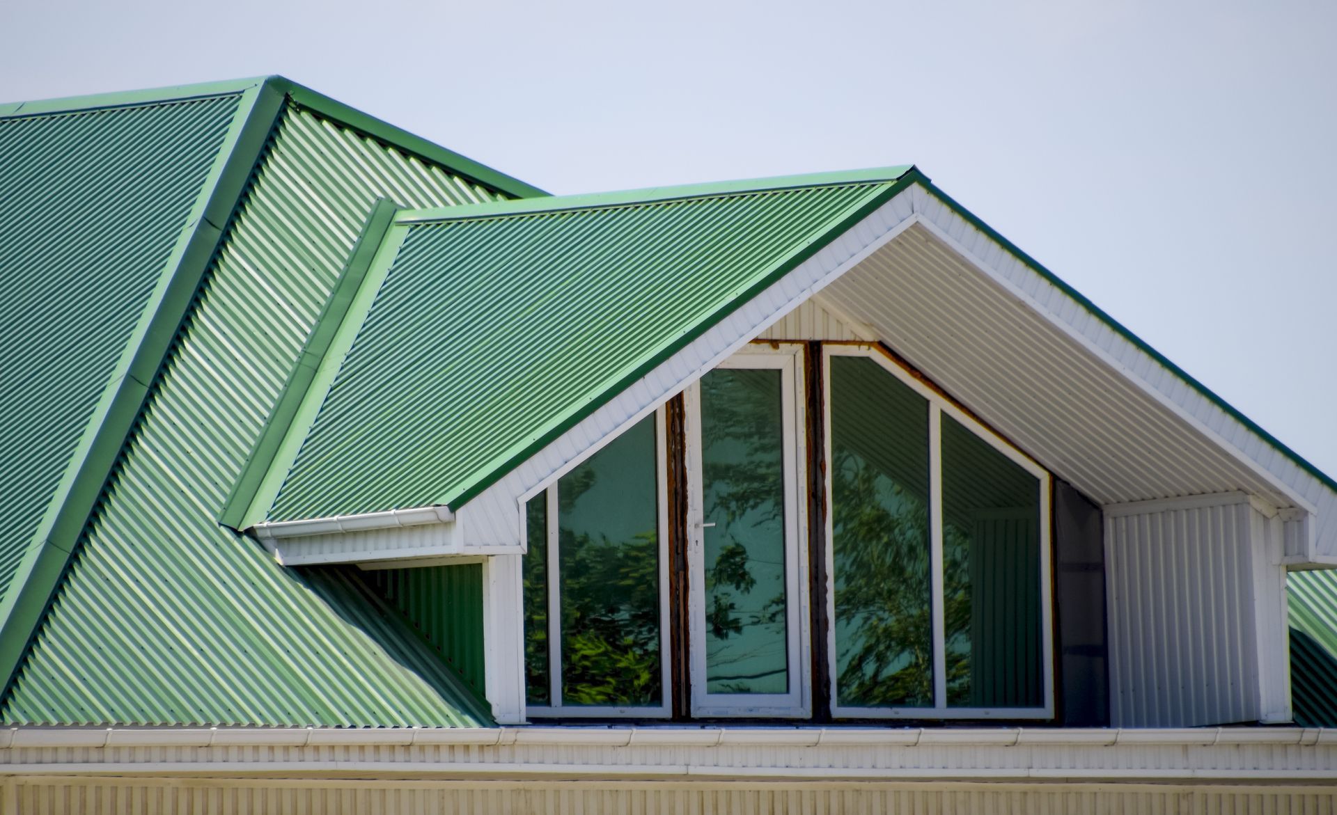 Green corrugated metal roof with white-framed windows reflecting trees — Ace Metal Roofing in Coffs Harbour, NSW