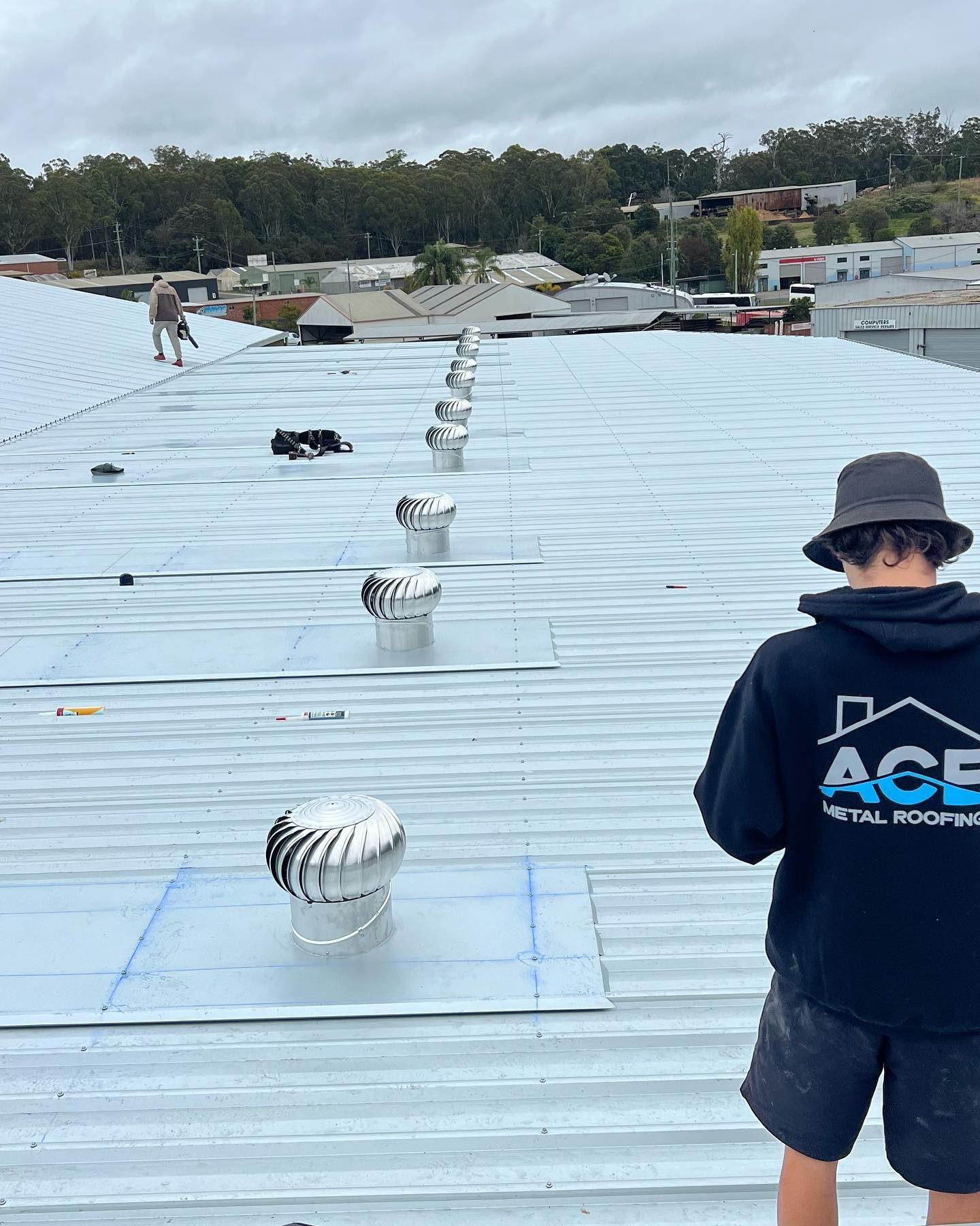 Workers Installing Roof Vents on a Corrugated Metal Roof Under a Cloudy Sky — Ace Metal Roofing in Waterview Heights, NSW