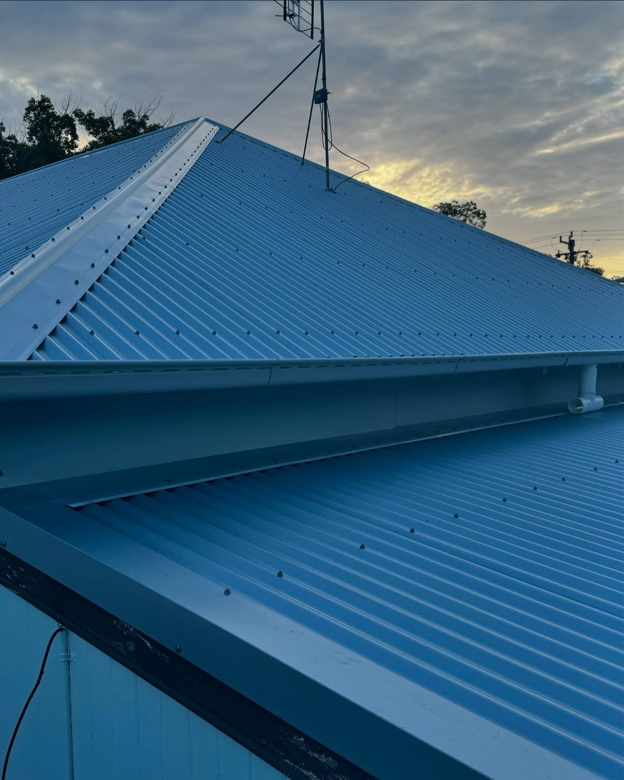 Corrugated Metal Roof With an Antenna Against a Cloudy Sky — Ace Metal Roofing in Waterview Heights, NSW