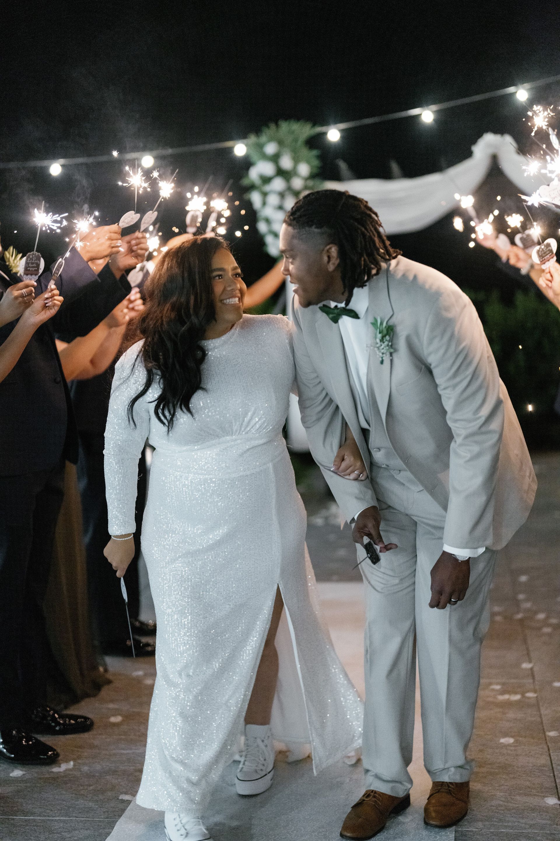 A bride and groom are walking through a crowd of people holding sparklers. wedding planner. stress free.