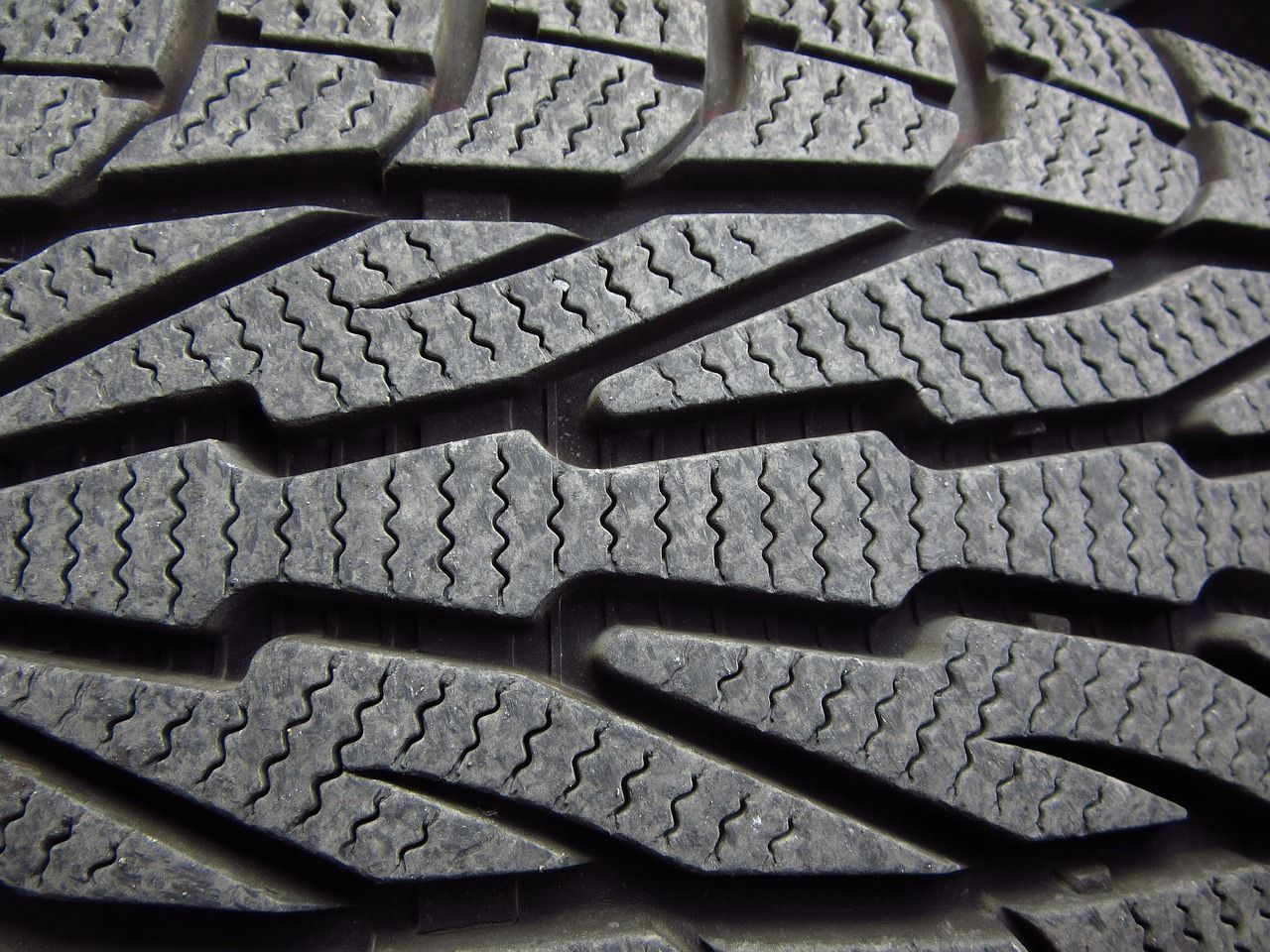 Close-up of a black tire tread with a patterned design of zigzag grooves and blocky rubber sections.