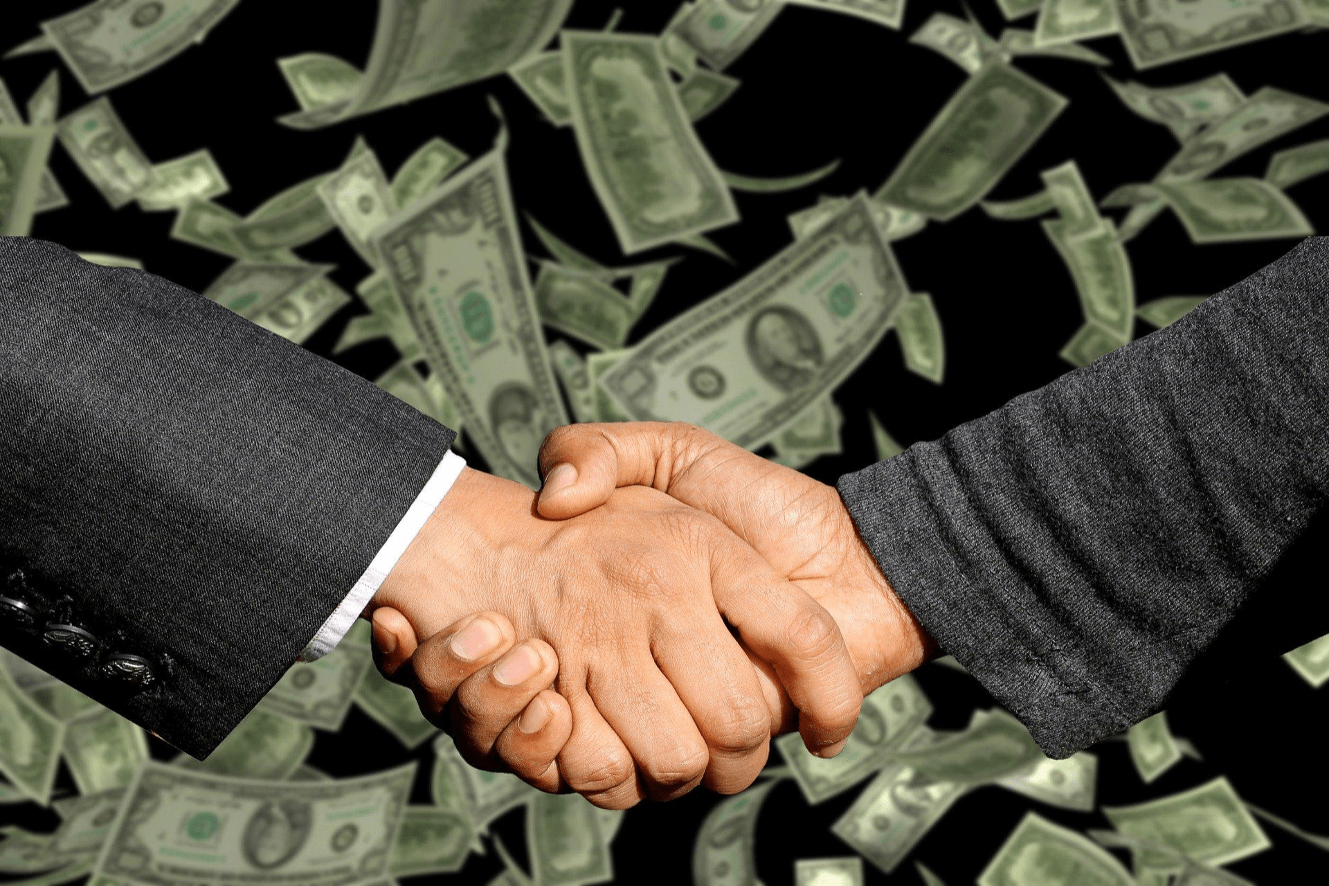 Two business people shaking hands, money falling in background.