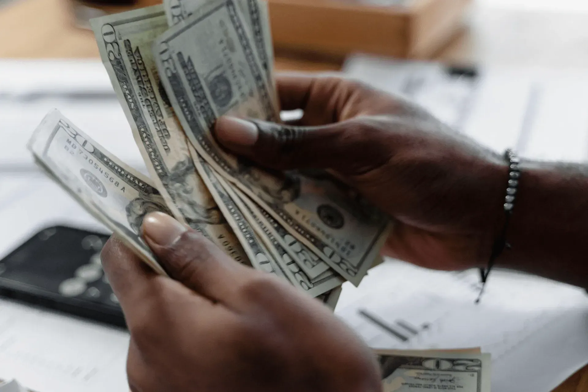 Hands counting a stack of US dollar bills.