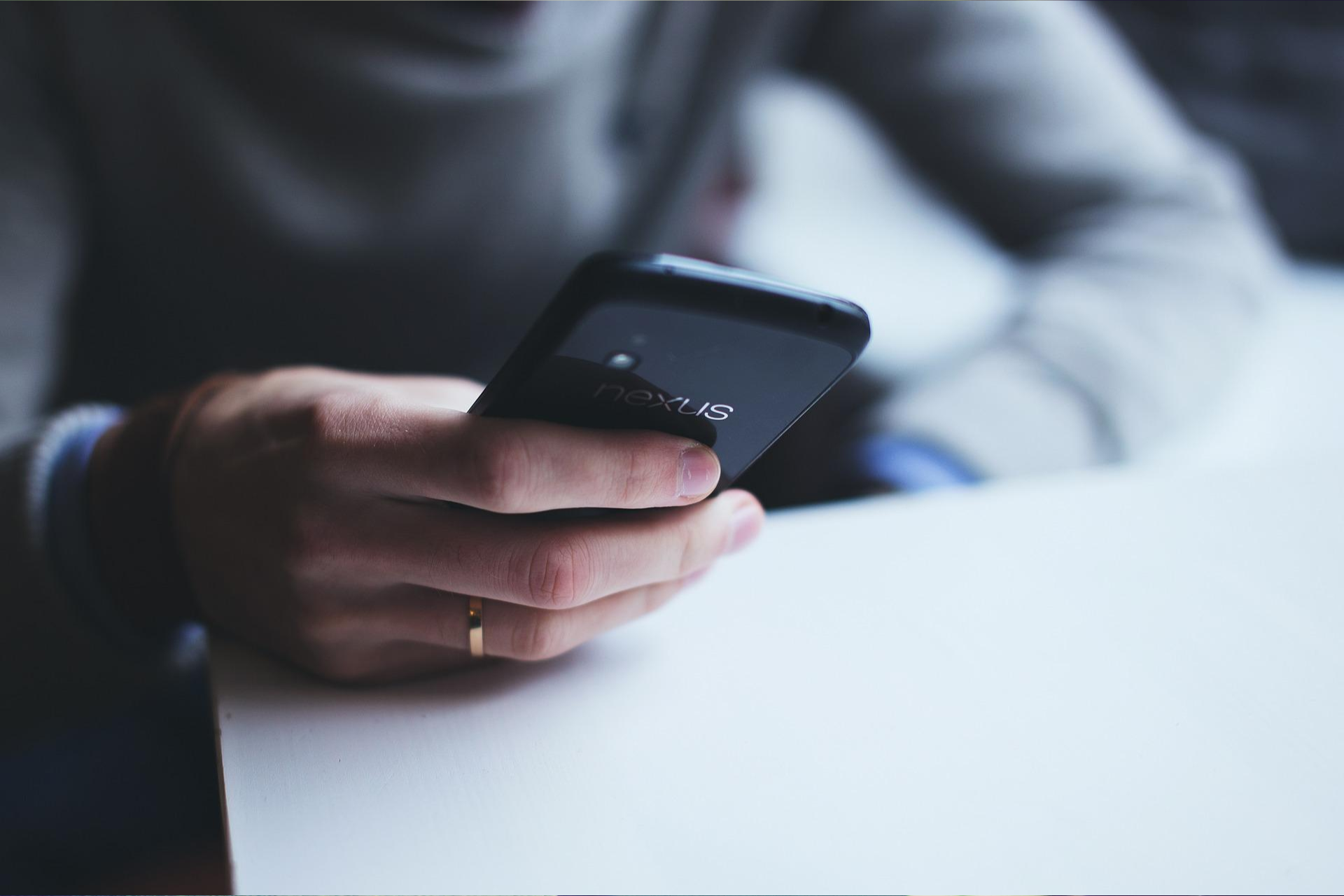 Person holding a black smartphone, resting on a white table.