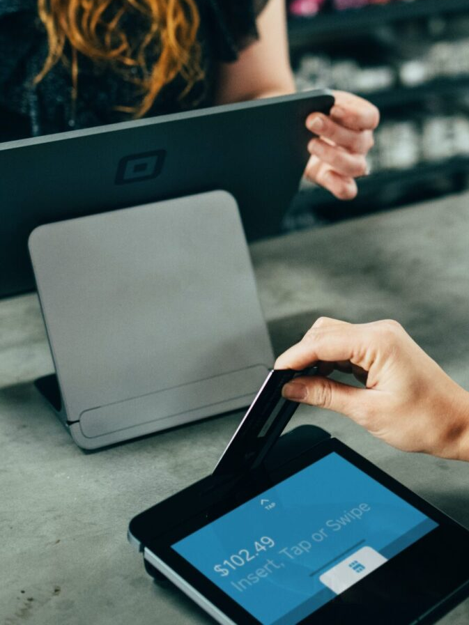 A customer inserting a credit card into a point-of-sale terminal at a store, the screen reads