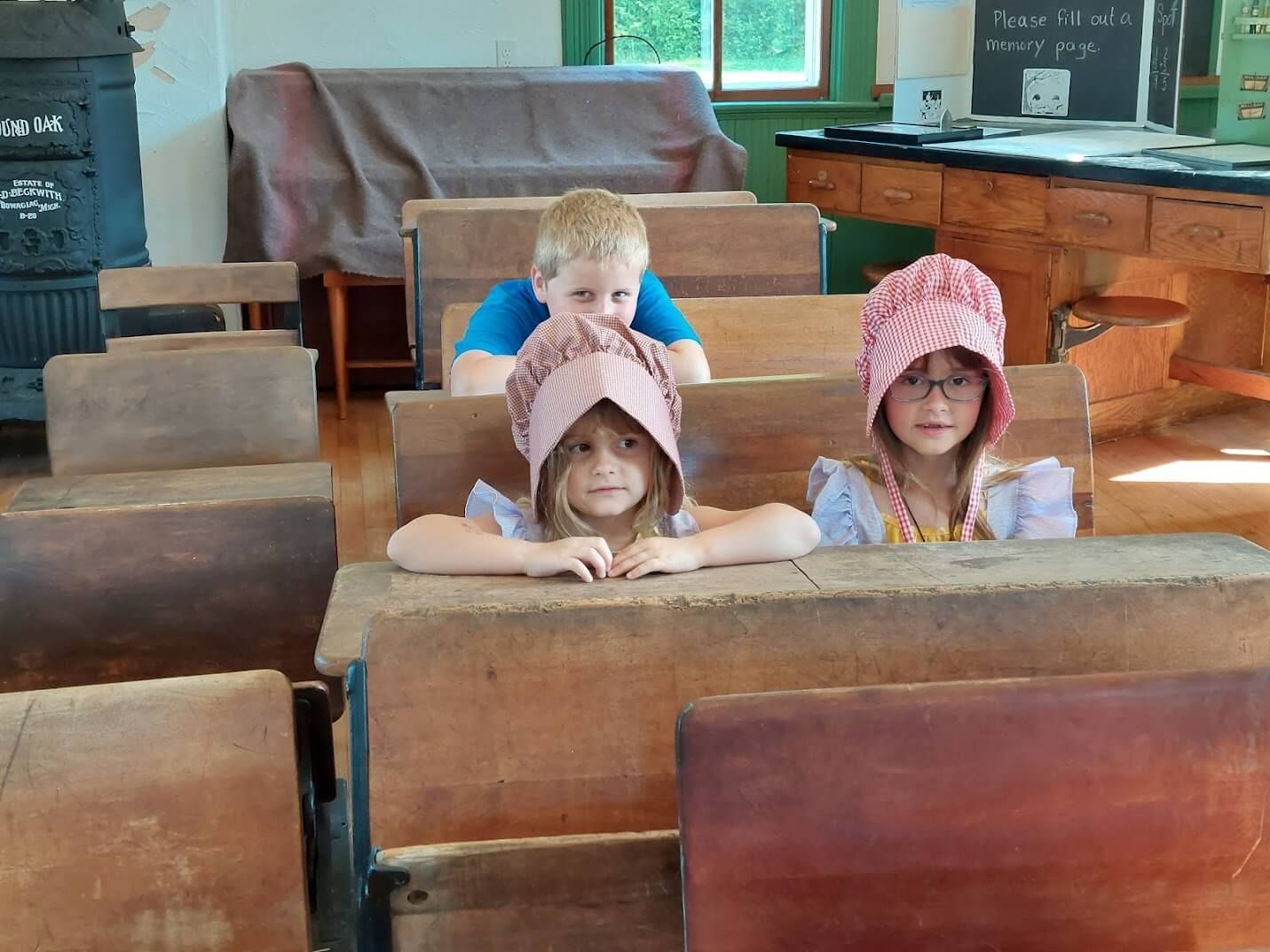 A boy and two girls are sitting at wooden desks in a classroom