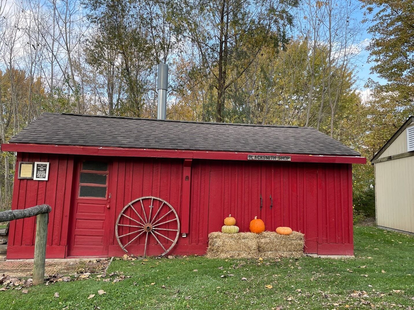 A red barn with pumpkins and hay bales in front of it.