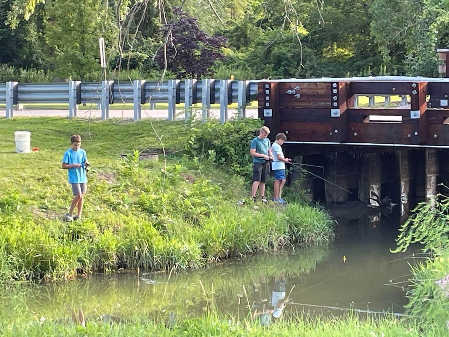 Two people are fishing in a river near a bridge.