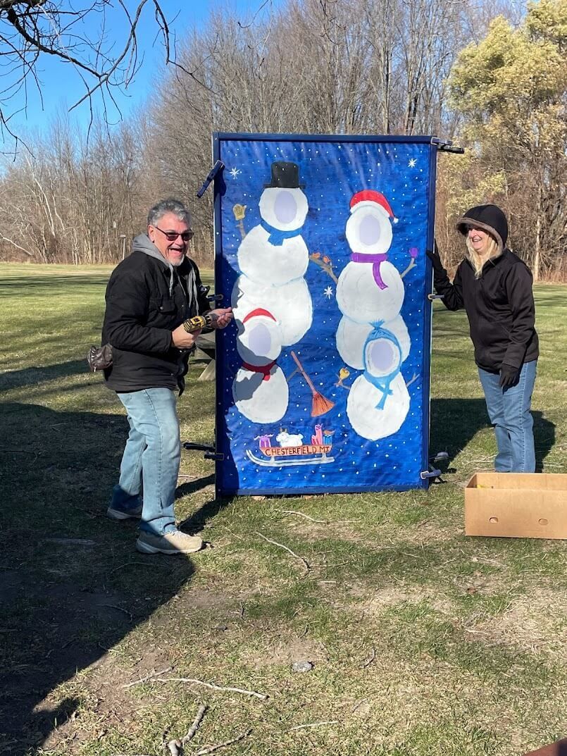 A man and a woman are playing a game with snowmen in a park.