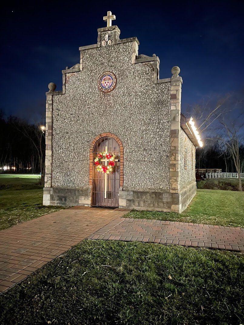 A small stone church with a cross on top of it is lit up at night.